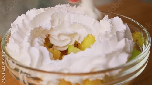 Whipped cream pouring on fruit salad in a bowl close up