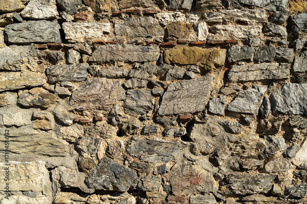 Fototapeta premium Textured stone wall features a variety of rock sizes and shapes, displaying natural colors and intricate patterns, perfect for use as backgrounds or architectural design elements in creative projects