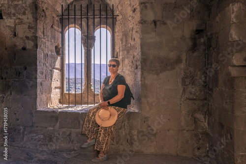 Woman posing with a hat in her hand in a medieval window of Loarre Castle in Huesca, Aragon, Spain