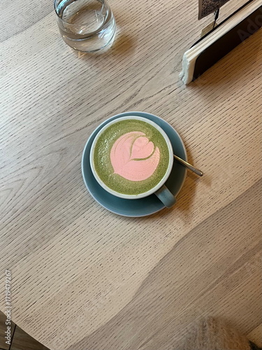Flat lay of matcha latte in cup with strawberry and latte art, and glass of water on cafe table, cozy autumn morning