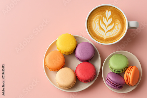 Multicolored French macarons on a plate, next to a cup of cappuccino with a pattern on a light pink background. Top view.