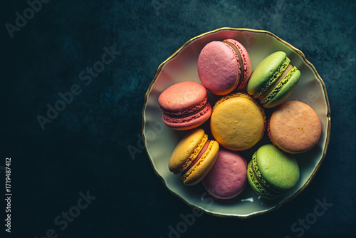 Multicolored French macarons in a plate against a black vintage background. Top view.