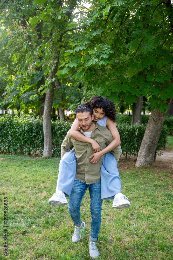 Naklejka premium Interracial couple having fun in the park, piggyback ride and laughter