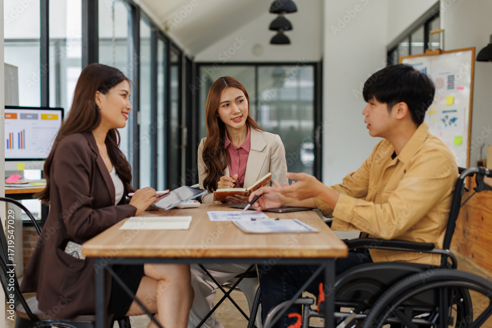 Fototapeta premium An inclusive modern office environment with a diverse team collaborating. A person in a wheelchair actively engages with colleagues. 
