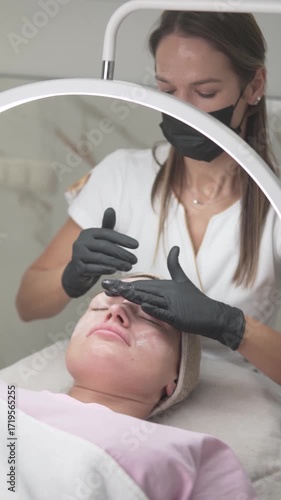 A beautician in gloves gently cleanses a woman is face before a skincare procedure at a professional beauty salon. This step ensures the skin is prepared and free of impurities for optimal treatment