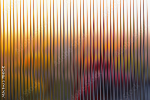 Abstract vertical ribbed glass texture with blurred warm sunset colors and hints of purple and pink hues creating a dreamy atmospheric effect
