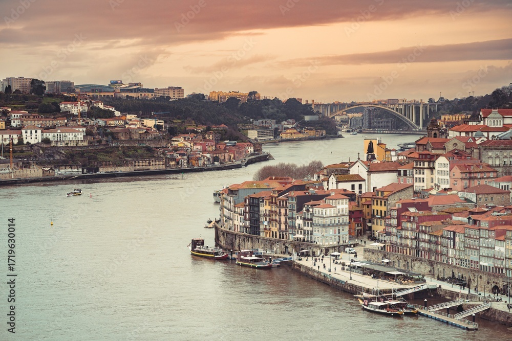 Fototapeta premium Overlooking the vibrant city as the light fades, the Douro River reflects the colors of the sky near the Dom Luis I bridge in Porto, Portugal