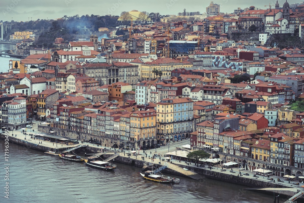 Obraz premium Views of the Ribeira district in Porto, Portugal on a cloudy day. People stroll along the river Douro and traditional boats are moored at the quayside