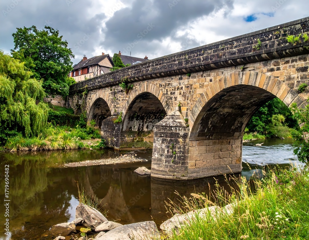 Fototapeta premium Stone arch bridge over a river with trees and houses