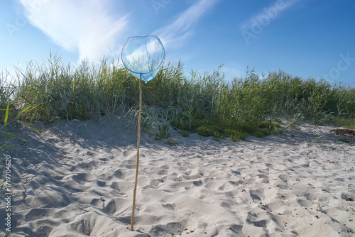 Blue landing net with wooden pole on a sandy beach, with a blue sky. Vacation