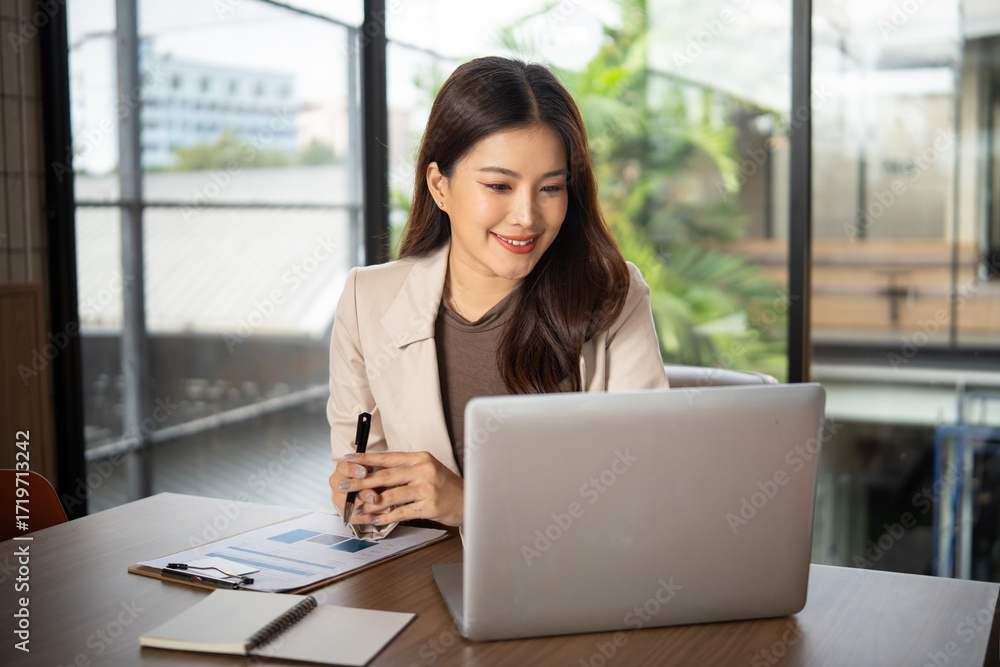 Fototapeta premium Confident businesswoman smiling while working on her laptop in a modern office.