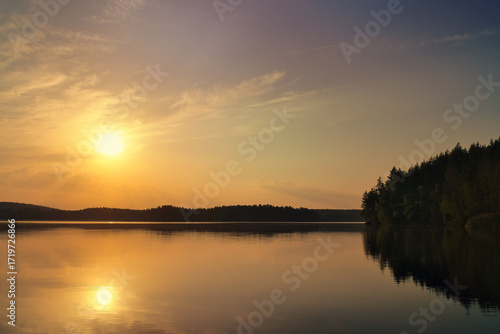 Sunset at the lake with reflection and forest, peaceful evening atmosphere