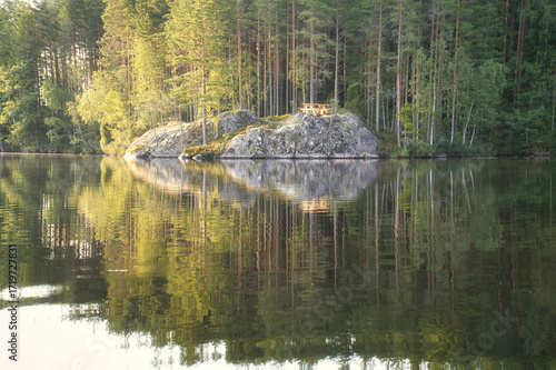 Lake landscape with a rocky island and a picnic table, surrounded by forest