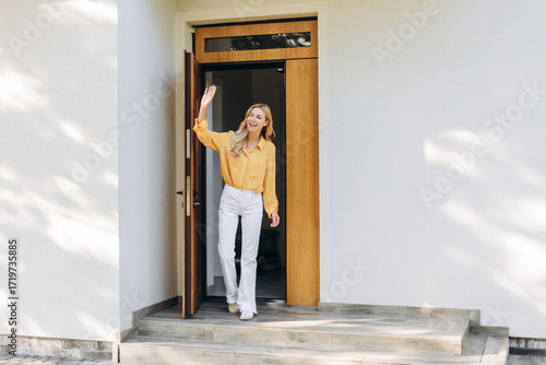 Fotografie Happy woman waving goodbye at front door of modern home