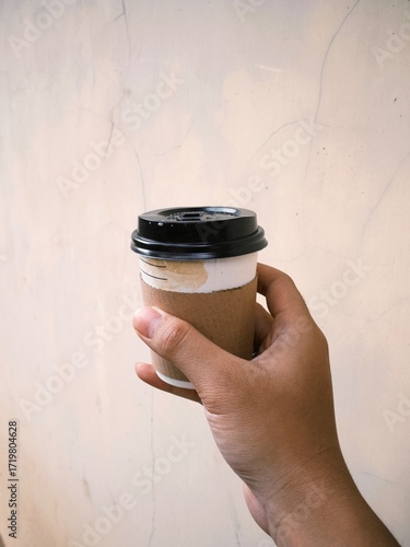 Hand holding a cup of coffee in disposable or take away packaging