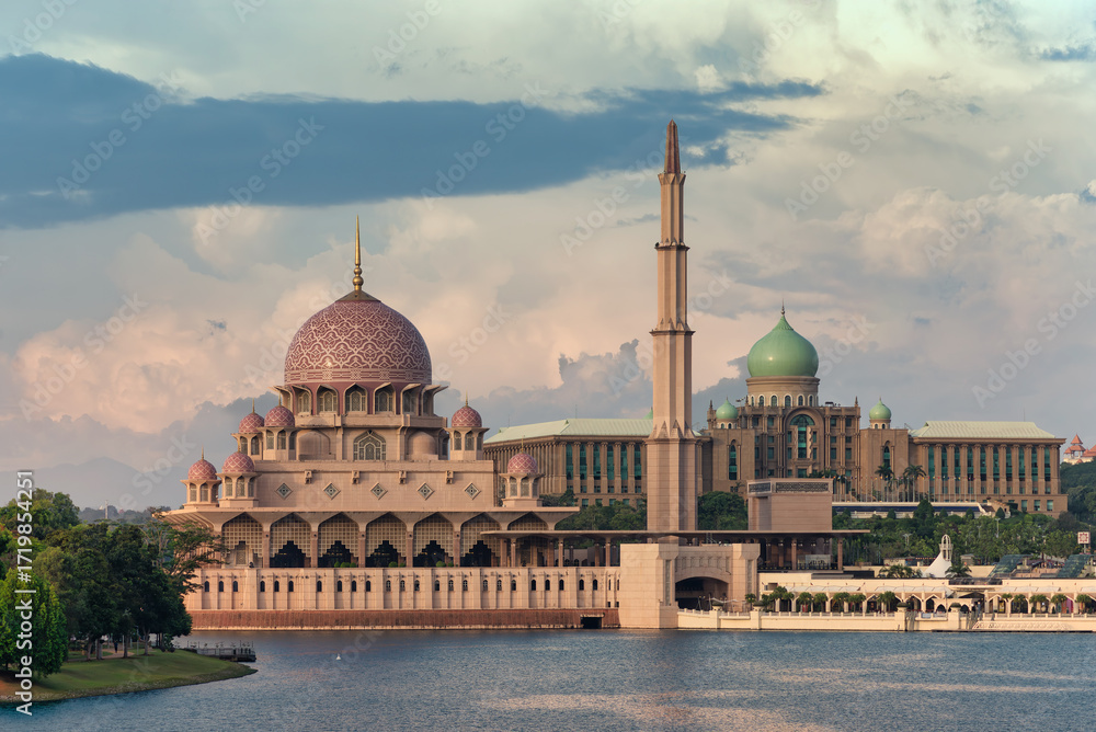 Obraz premium Putra Mosque, pink dome, and Perdana Putra, green domes, across Putrajaya Lake, Putrajaya, Malaysia. Iconic architecture under a cloudy sky in golden hour