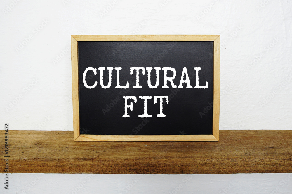 Fototapeta premium Cultural Fit text written on blackboard with wooden shelf and concrete background