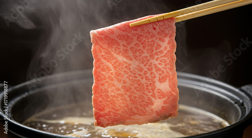 Chopsticks holding marbled Wagyu beef over a steaming Sukiyaki hot pot