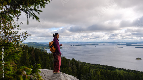 Obraz na plátně A woman stands on a rocky ledge in Koli National Park, admiring the breathtaking