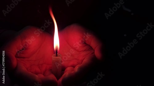 Close-up of a hand holding a lit candle in the dark background.