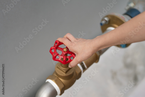 Obraz na plátně Close up of a person turning a red valve handle on a brass water pipe system