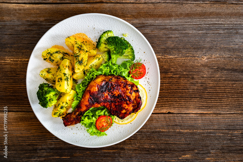Oven roasted chicken leg with boiled potatoes and boiled broccoli on wooden table	