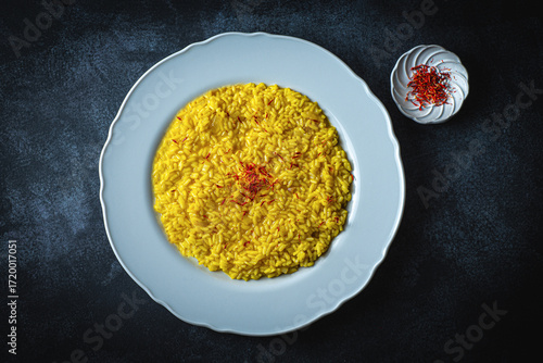 Risotto alla Milanese in a white aristocratic dish on the dark table. A classic Lombard saffron risotto recipe. Cuisine the North Italy