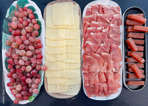 Top view on large platters of cheese, ham and other cold meats with large grapes.  