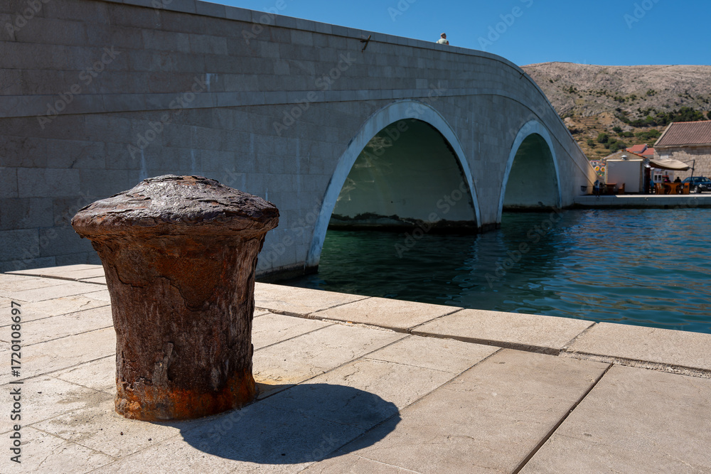 Naklejka premium Rusty Mooring Bollard and Stone Arch Bridge in Pag Croatia