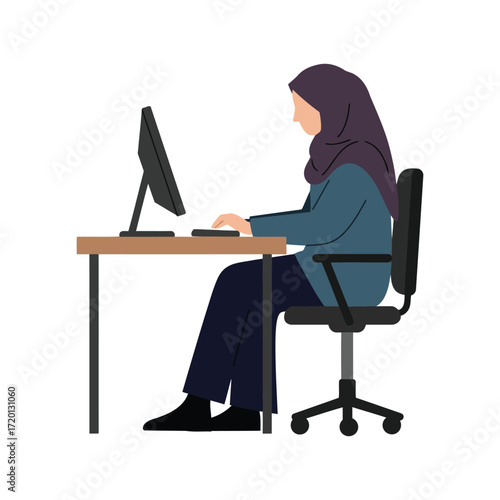 A woman wearing a hijab sits at a desk, typing on a keyboard while looking at a computer monitor in an office setting.