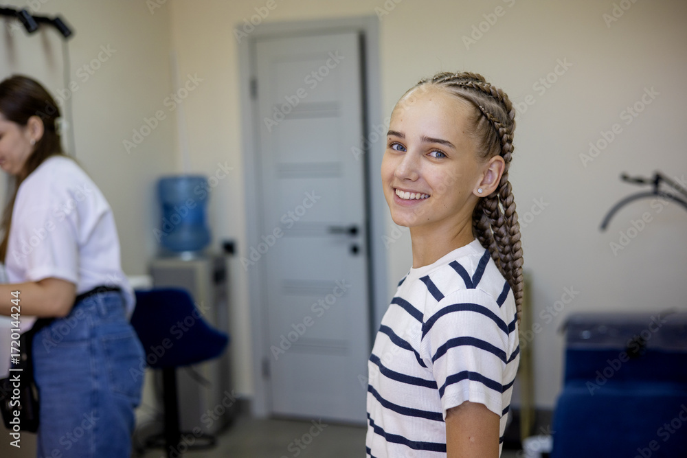 Obraz premium Smiling girl with braided hair in a bright salon during a lively hair styling session