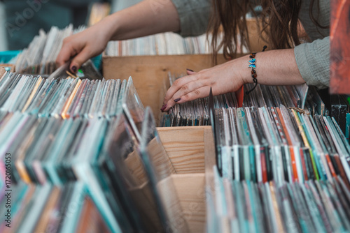 Girl browsing vinyl records in wooden crates at a music store or flea market. Close-up of hands flipping through vintage LP albums, symbolizing retro music culture, nostalgia and collecting
