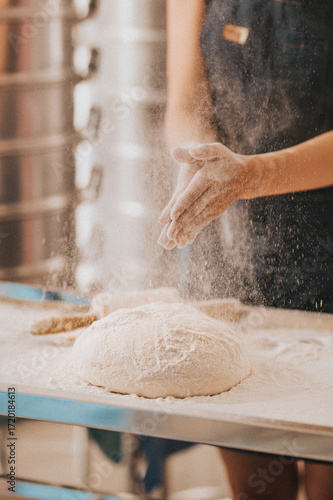 A baker dusts flour over a dough ball, capturing the art of baking in a cozy kitchen setting.