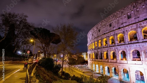 The colosseum illuminated at night with light trails from passing cars