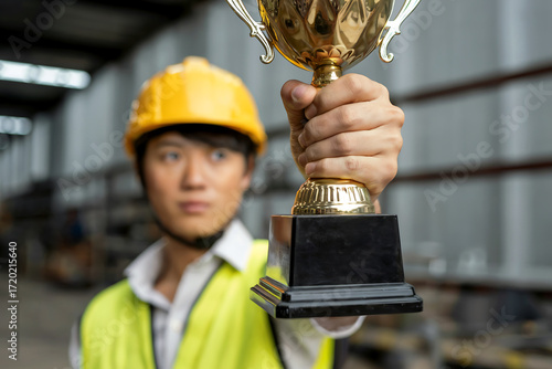 Asian man in yellow hard hat and safety vest holding gold trophy male award