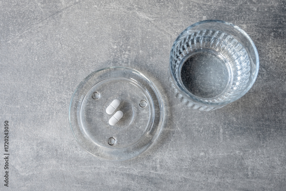 Obraz premium White pill and glass with water stay on the table.