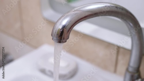 Close-up of water flowing from a chrome bathroom faucet into a white sink, ideal for home improvement and plumbing projects.
