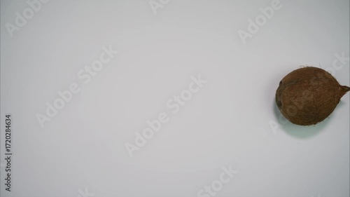 One coconut comes in the middle of the frame, spins and leaves the frame on white background. Stop motion animation