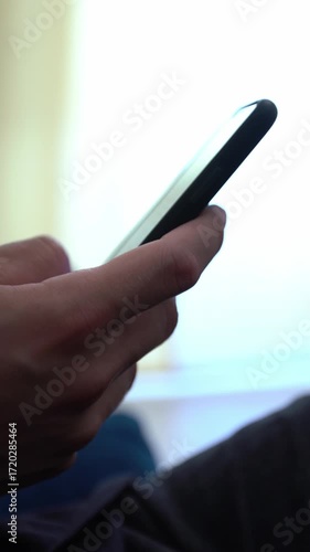 Caucasian man using smartphone, sitting on sofa at home. Male hand touching screen cell phone in the interior house. Surfing internet, checks social network and write text on device mobile