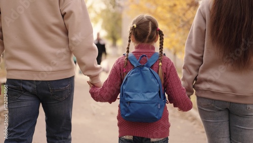 Bild auf Leinwand small child with backpack holds mother and father by hand, kid with mom and dad walks around schoolyard after school, happy family, rush to first call, primary education, school bag on baby shoulders