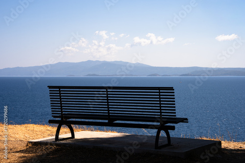 Wooden bench on a viewpoint in Sithonia, Greece, overlooking the sea. Peaceful coastal landscape with panoramic views of the Mediterranean.