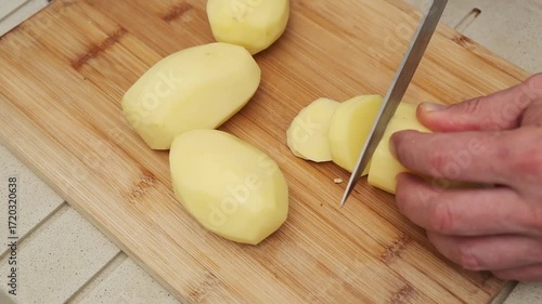 Fresh potato slicing on wooden cutting board for culinary preparation.