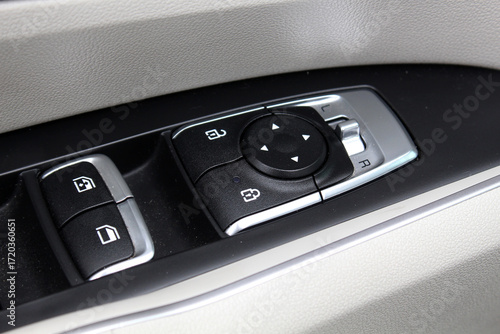 Photography Car door control panel with black buttons and silver trim, featuring power window switches, door lock controls, and side mirror adjustment knob with directional arrows