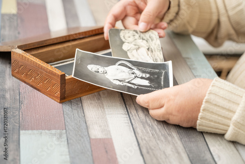 Fotografia Hands holding vintage black and white photo baby family archive near wooden box,