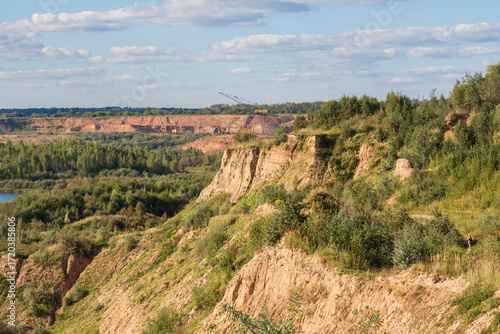 A scenic view of rugged cliffs covered with green vegetation overlooking a forested valley under a partly cloudy sky on a sunny day.