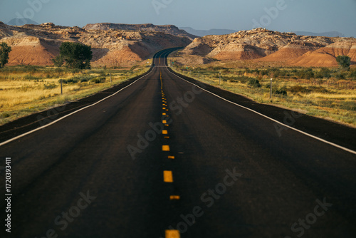 A winding road stretches through vibrant landscapes and rocky terrain under blue sky.