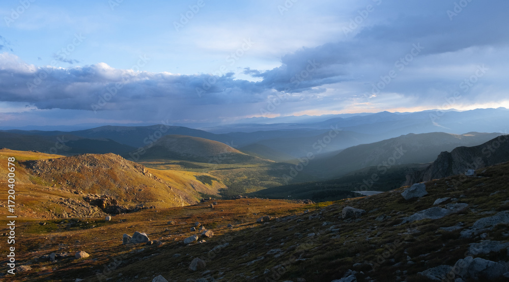 Obraz premium Sun rays breaking through clouds over mountain valley, scenic wilderness landscape with rolling hills and dramatic light