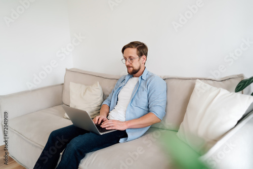 Fotografie Young businessman types on laptop at home, representing remote flexibility, concentration, and integration of digital tools in modern freelance or entrepreneurial routine
