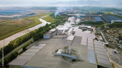 Aerial view of industrial factory with chimney smoke rising, highlighting air pollution and environmental impact in an urban industrial landscape.
