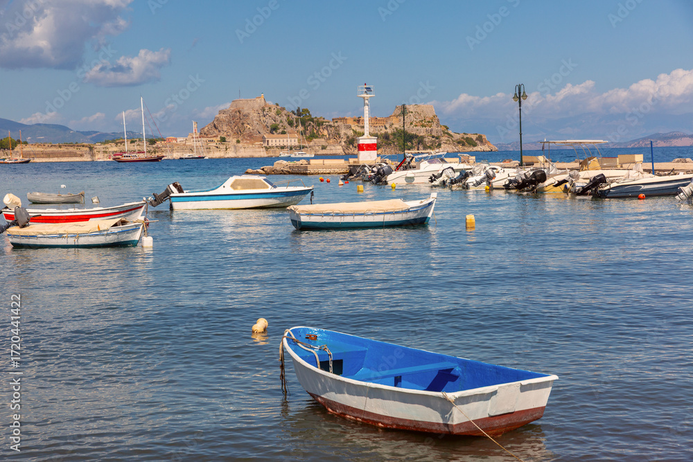 Fototapeta premium Small boats moored in marina with view of Old Fortress in Corfu Greece in sunny day
